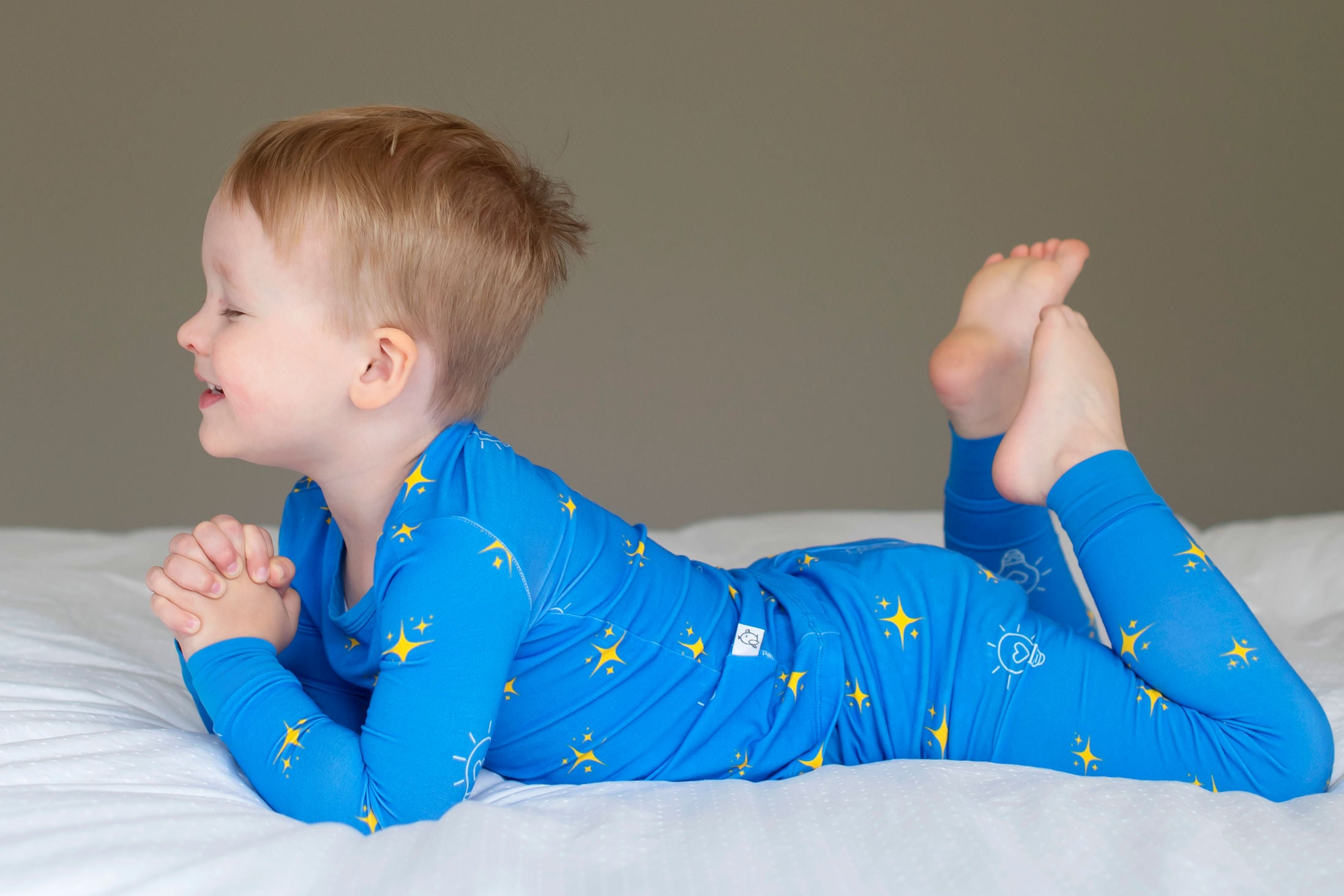 Child wearing blue pajamas with star patterns on a white bed against a plain background
